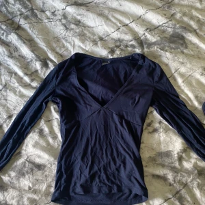 Marinblå v-ringad topp - Snygg marinblå långärmad och v-ringad topp från Gina Tricot i storlek XS. Använd fåtal gånger och jag säljer då den inte kommer till användning 🤍 den har i slutet på ärmarna hål för tummarna 🧐 men inget jag tycker märks av vid användning 