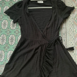 Svart omlottklänning med volang - Supersöt svart omlottklänning från Zara med korta ärmar och knytband i midjan, så man kan även använda den som en kofta🫶🏻