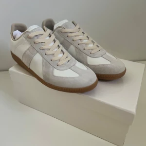 Maison Margiela sneakers i mocka och skinn - Snygga sneakers från Maison Margiela i beige och vitt med ovandel i mocka och skinn, klassisk gummisula och beige snörning. Stilren och tidlös design som passar perfekt till jeans eller dressade byxor.