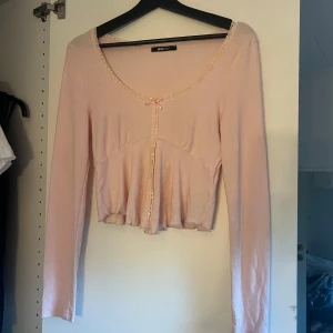 Ljusrosa topp Gina Tricot - Supersöt ljusrosa topp från Gina Tricot med långa ärmar. Toppen har spetsdetaljer längs ringningen och framtill samt en liten rosett vid halsen. 
