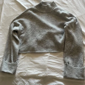 Grå croppad stickad polotröja - Croppad grå stickad tröja med ribbad hög krage från Gina tricot. Tröjan är välanvänd och har lite noppor, men inget som stör helhetsintrycket🩷
