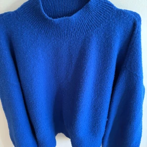 Blå stickad tröja från & Other Stories - Superfin blå stickad tröja från & Other Stories med hög ribbad krage och långärmad modell. Perfekt för lager-på-lager och ger en snygg pop av färg till din outfit. Mjuk och skön känsla, passar dig som gillar en klassisk men trendig look.