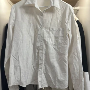 Vit skjorta från SHEIN i storlek L - Klassisk vit skjorta från SHEIN i storlek L. Skjortan har lång ärm, bröstficka och knappar framtill. Den har en rak passform och är perfekt att styla med jeans eller kostymbyxor.