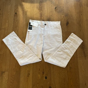 Beige tapered linnebyxor Jack & Jones - Snygga ljusbeige linnebyxor från Jack & Jones med tapered passform. Byxorna har klassiska sidfickor, bälteshällor och knäppning fram. Perfekta för en chill och stilren look under varmare dagar. Storlek: waist: 28, leg: 30.    Nypris: 599,95kr