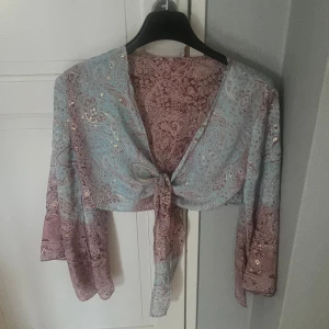 Blus med knytning - Superfin blus med ljusblå och lila toner. Köpt i Grekland. Modellen är croppad med långa, vida ärmar och knyt framtill. Storlek S/M!                 Skriv vid frågor🫶🏻