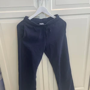 Mörkblå mjukisbyxor från Gina Tricot - Mörkblå mjukisbyxor från Gina Tricot med resår och snörning i midjan. Byxorna har raka ben och är tillverkade i mjukt bomullsmaterial. Perfekta för chill dagar eller när du vill vara extra bekväm.