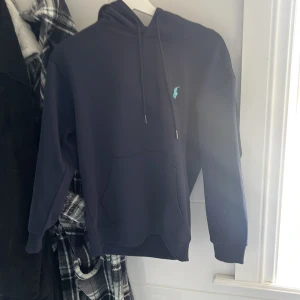 Mörkblå hoodie från Polo Ralph Lauren - S men sitter som xs. Säljer en mörkblå hoodie från Polo Ralph Lauren med klassisk huva och snörning. Tröjan har en broderad logga i ljusblått på bröstet och en stor magficka. Perfekt för dig som gillar stilren och sportig look.