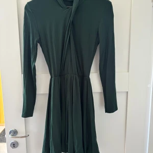 Mörkgrön klänning med bälte - Supersnygg mörkgrön klänning med lång ärm och tillhörande bälte med silverdetalj. Klänningen har markerad midja, lätt rynkad kjol och är i ett mjukt, flowy material. 