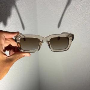  CHIMI solglasögon  - Snygga solglasögon från CHIMI med transparent beige båge och fyrkantig form. Glasen är mörktonade och ger en cool vibe. Ramen är i plast och designad i Stockholm. Perfekta för att lyfta din stil i sommar.