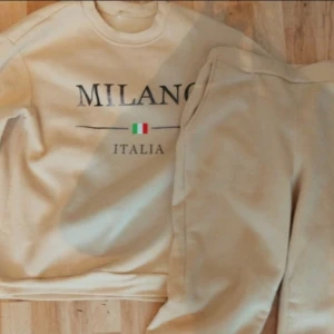Beige sweatshirt Milano Italia - Beige sweatshirt med texten 'MILANO ITALIA' och en liten italiensk flagga framtill. Tröjan har rund hals och lång ärm, perfekt för en chill och avslappnad stil. Mjuk och skön, passar till både jeans och mjukisbyxor.