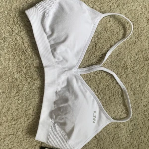 Vit seamless sporttopp från ICANIWILL - Minimalistisk vit sporttopp från ICANIWILL med tunna axelband och sömlös design. Toppen har ribbade detaljer på sidorna och bred resår under bysten för extra support. 