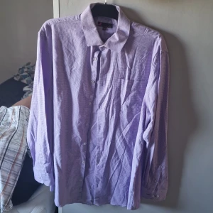 Lila rutig skjorta från Dressmann 2XL - Snygg lila skjorta från Dressmann i storlek 2XL med diskret rutigt mönster. Skjortan har klassisk krage, bröstficka och knäppning framtill. Perfekt för dig som gillar en stilren look med lite färg. Långärmad och passar till många olika outfits.