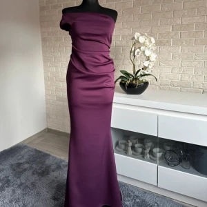 Oneshoulder balklänning - Snygg långklänning i en djup lila nyans med offshoulder-design. Klänningen har en figurnära passform och draperade detaljer över byst och midja som ger en cool och elegant look. Skriv för mått☺️