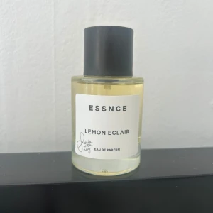 ESSNCE Lemon Eclair parfym - Fräsch parfym från ESSNCE med doften Lemon Eclair. Kommer i en stilren, rund glasflaska med svart lock och vit etikett. Parfymen har en ljusgul vätska som ger en fräsch och citrusaktig känsla. Helt oanvänd 