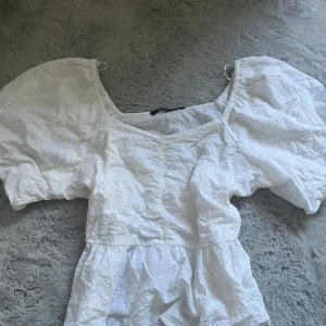 Vit blus med puffärm från KappAhl - Superfin vit klänning från KappAhl med broderade små blommor och puffiga korta ärmar. Klänningen har en söt, romantisk look med markerad midja och lätt volang nedtill. Perfekt för sommarens alla tillfällen!