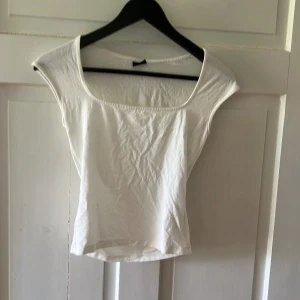 Vit topp med bred ringning Gina Tricot - Enkel och stilren vit topp från Gina Tricot i storlek XS. Modellen är kortarmad med bred ringning och rak passform. Perfekt att matcha med jeans eller kjol för en clean look. Gjord i mjuk bomull som känns skön mot huden.