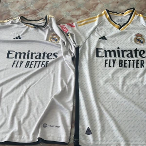 Real Madrid hemmatröja 23/24 Adidas - Säljer en officiell Real Madrid hemmatröja från säsongen 23/24. Tröjan är vit med subtilt mönster, svarta detaljer och guldiga ränder på axlarna. Broderad klubbmärke och Adidas-logga, samt 'Emirates Fly Better' tryckt på bröstet. Tillverkad i lätt funktionsmaterial. För båda 550