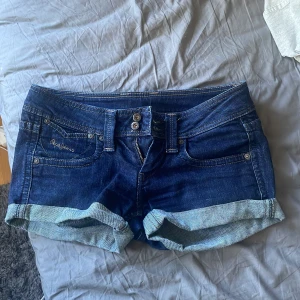 Lågmidjade jeansshorts - Snygga mörkblå jeansshorts från Pepe Jeans med uppvikta benslut och klassiska fem fickor. Shortsen har dubbla knappar och dragkedja framtill samt broderad logga på fickan. Perfekta för sommardagar och enkel att matcha med allt. Skriv om ni har några frågor eller något💞Jag säljer dem för att dem är tyvärr för stora💞Midjemåttet är ca 38/39 och priset kan alltid diskuteras!! 