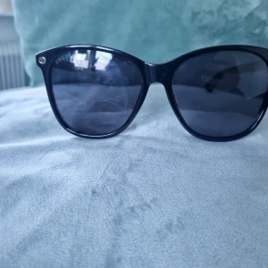 Svarta solglasögon från Gucci - Snygga svarta solglasögon från Gucci med klassisk form och mörka glas. Diskret guldfärgad Gucci-logga på skalmen. Tillverkade i Italien och har en stilren design som passar till många outfits. NYPRIS 2098 SEK