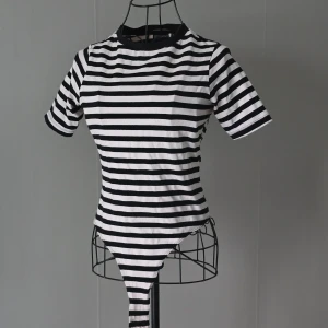 Randig svartvit bodysuit topp - Säljer en randig svart och vit bodysuit topp med korta ärmar och rund hals. Toppens design är tight och den har klassiska horisontella ränder.