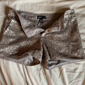 Glittriga paljettshorts från Mango - Snygga shorts från Mango i storlek 36, täckta med silvriga paljetter som ger en riktigt festlig look. De är fodrade på insidan för extra komfort och har en klassisk passform med midja och dragkedja. Perfekta för dig som vill sticka ut och glänsa på fest!