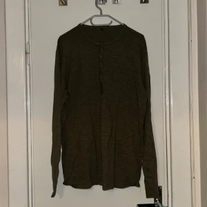 Olivgrön långärmad tröja med knappar  - Olivgrön långärmad tröja i mjuk bomull med rund halsringning och knappslå framtill. Enkel och stilren modell som passar perfekt till jeans eller chinos. Tröjan har en relaxed fit och är riktigt skön att bära.