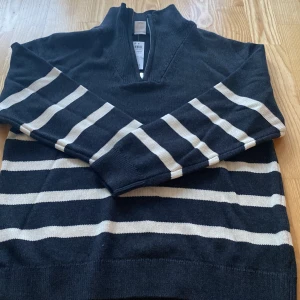 Randig half zip tröja från Lindex - Mörkblå och vit randig tröja från Lindex med half zip och hög krage. Tröjan har långa ärmar och är stickad i mjukt material, perfekt för kyligare dagar. Snygg och enkel att matcha med jeans eller kjol.