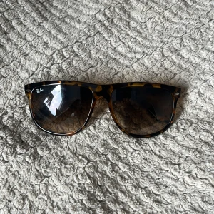 Ray-Ban Wayfarer solglasögon brunmelerad - Snygga Ray-Ban Wayfarer solglasögon med brunmelerad båge och mörka glas. Klassisk modell med coolt mönster och ikonisk logga på linsen. Perfekt accessoar för att lyfta din stil.