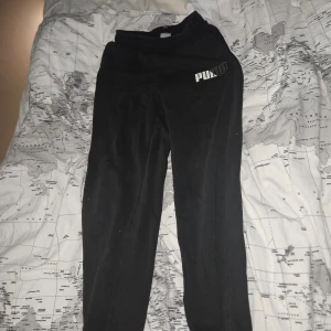 Svarta mjukisbyxor från Puma - Svarta mjukisbyxor från Puma med vit logga på vänster lår. Byxorna har resår i midjan och är tillverkade i mjukt bomullsmaterial. Perfekta för chill eller träning, med en klassisk och enkel look. (Dessa är i barn storlek så rekomderas för barn)