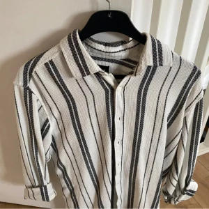 Randig skjorta pull&bear - Säljer en snygg randig skjorta/overshirt från Pull&Bear i storlek M. Skjortan har ett stilrent mönster i svart och vitt med knappar framtill. Perfekt för både vardag och fest! 🖤🤍Hör av er vid frågor eller om du vill ha fler bilder. 👊