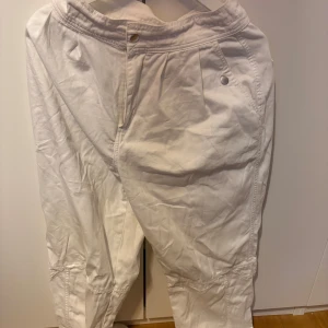 Vita loose-fit byxor med detaljer - Säljer ett par vita byxor med avslappnad passform och snygga sömdetaljer vid knäna. Byxorna har hög midja, knappstängning och fickor fram. Perfekta för en chill och stilren look.