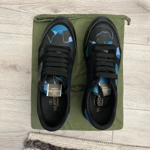 Valentino Garavani Rockrunner sneakers - Snygga Valentino Rockrunner sneakers med svart och blått kamouflagemönster. Skorna har svarta snören, platt sula och detaljer i både skinn och mocka. Perfekt för dig som vill sticka ut med en exklusiv och trendig look.