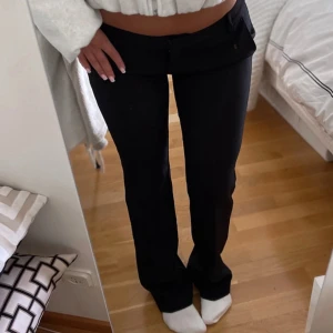 Svarta lågmidjade bootcut byxor - Säljer ett par svarta lågmidjade byxor med bootcut-snitt. Byxorna har klassisk look med fickor fram och stängs med dragkedja och knapp. Perfekta om du gillar en trendig och stilren vibe. Materialet känns mjukt och följsamt.
