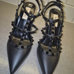 Valentino garavani pumps - Eleganta svarta Valentino Garavani pumps i läder med ikoniska nitar. Perfekt för både fest och vardag. Levereras med originalkartong och dustbags. Storlek 39, ca 11cm klack, köpt juni 2024 och användes aldrig. Köpt för 10.400:- kvitto finns