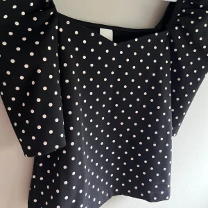  prickig topp  - Svart topp från H&M med vita prickar och lite puffiga trekvartsärmar. Snygg v-ringning och rak passform. Säljer pga att jag köpte helt fel…🩷 så denna passade inte ens mig🩷 skriv privat för ytligare bilder eller frågor! 