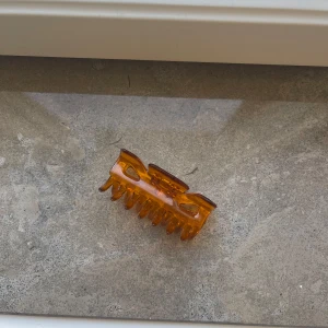 Brun hårklämma  - En snygg hårklämma i transparent brun plast med klassisk retrokänsla. Klämman har rejäla taggar och en stadig fjäder, perfekt för att hålla upp håret på ett stilrent sätt. Passar både till enkla och mer stylade frisyrer.