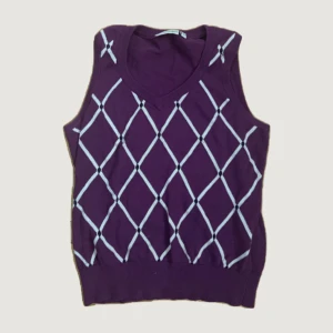 Lila rutig stickad väst Cappuccini - Snygg lila stickad väst från Cappuccini i storlek S. Västen har ett rutigt mönster i vitt och v-ringad hals. Perfekt att styla över en skjorta eller t-shirt för en trendig look.