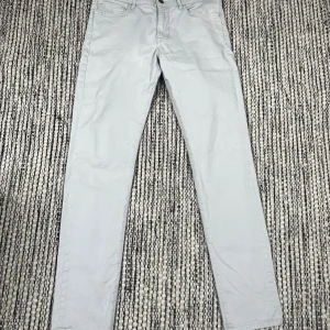 J.lindeberg Ljusgrå chinos perfekta för golf   - Snygga ljusgrå chinos från J.Lindeberg i lite slimare rak modell. Bredden är 33 men sitter som en 31 o längden är 34 men sitter som en 32. Stängs med dragkedja och knapp. Tillverkade i mjuk bomull som känns skön mot huden. Perfekta för en clean och stilren look.     Om du vill ha mått eller fler bilder är det bara att skriva!