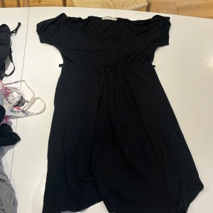 Svart kortklänning från ICHI - En svart kortklänning från ICHI med korta ärmar och markerad midja. Klänningen har en enkel och stilren design med rundad halsringning och mjukt, följsamt tyg som ger en skön passform.