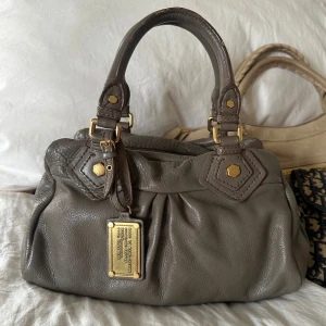 Beige Q Classic Baby Groove väska! - Bättre pris fås vid köp via min vinted istället @juliavallberg 🤍 Snygg beige/grå väska i fint skick från Marc by Marc Jacobs i äkta läder med gulddetaljer och handtag. Något slitet vid handtagen som syns på bilden. Men det är en välbevarad vintage modell! Perfekt för att ge en stilren touch till din outfit. Skriv privat för fler bilder. Mått 34x18x12 (undersida). Kan hämtas hemma hos mig i Nacka eller skickas men kan tyvärr inte mötas🤍