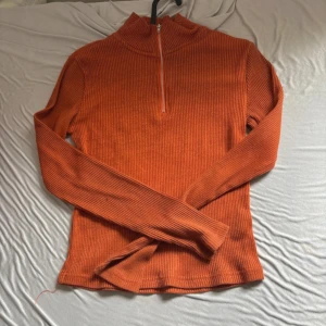 Orange ribbad tröja från Bik Bok - Säljer en orange ribbad långärmad tröja från Bik Bok med half zip framtill och hög krage. Tröjan är i stretchigt material och har en slim passform som sitter snyggt på kroppen. Perfekt för lager-på-lager under hösten.
