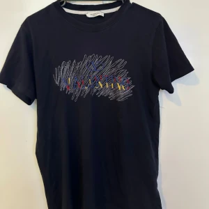 Svart Valentino t-shirt med broderi - Svart t-shirt från Valentino med färgglatt broderat logotyptryck i rött, blått och gult på bröstet. T-shirten har rund halsringning och korta ärmar. Materialet är mjuk bomull som känns skönt mot huden. Perfekt för dig som gillar exklusiva och snygga statement-plagg.