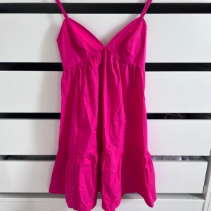 Rosa kortklänning med snörning - Supersöt rosa kortklänning från Bikbok med smala axelband, v-ringning och volang nertill. Baksidan har snygg snörning med två rosetter som ger en extra detalj. Perfekt för sommarens alla tillfällen och riktigt skön i bomull.