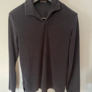 Mörkblå  långärmad pikétröja i frotté - En stilren mörkgrå pikétröja i frotté med lång ärm och klassisk krage. den är helt oanvänd.Tröjan har en enkel design utan synliga knappar och är perfekt för dig som gillar en clean look. Mjuk och bekväm, passar till många olika outfits. Tveka inte om du har frågor.