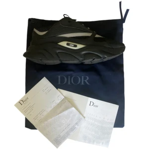 Dior B22 - Snygga chunky sneakers från Dior i svart med grå detaljer. Skorna har en kraftig sula, meshpartier och skinnpaneler för en modern look. Klassisk snörning och diskret Dior-logga på sidan. Perfekta för dig som gillar exklusiva och trendiga sneakers.