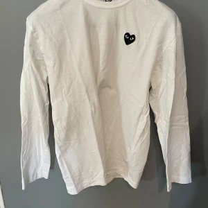 Vit långärmad tröja Comme des Garçons - Vit långärmad tröja från Comme des Garçons Play med det ikoniska svarta hjärtat broderat på bröstet. Enkel och clean design i mjuk bomull, perfekt för dig som gillar stilrena plagg med en twist. Storlek XL men passar bättre på L