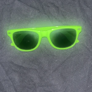 Neongröna solglasögon - Säljer ett par riktigt coola solglasögon i neongrönt med klassisk wayfarer-form. Perfekta för att sticka ut i mängden och ge din outfit en färgklick. Lätta och bekväma att bära hela dagen.