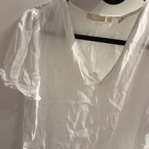 Vit blus med puffärm och v-ringning - Superfin vit blus med v-ringning och korta puffärmar. Tunt, lätt material som känns luftigt och perfekt för varmare dagar. Ärmsluten har resår för en söt volang-effekt. Enkel att styla till jeans eller kjol.