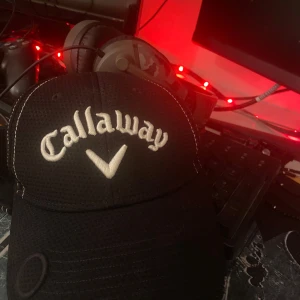 Svart Callaway keps med vit brodyr - Snygg svart keps från Callaway med vit brodyr framtill och Odyssey-logga bak. Kepsen är tillverkad i 100% polyester med ventilerande meshstruktur och har vita kontrastsömmar som ger en sportig look. Justerbar baktill för perfekt passform.