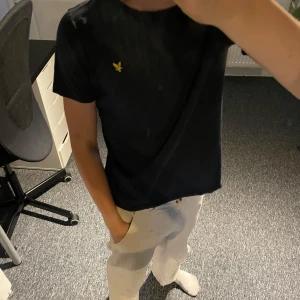 Svart t-shirt från Lyle & Scott - En stilren svart t-shirt från Lyle & Scott med klassisk passform och korta ärmar. T-shirten har det ikoniska gula fågel-loggan broderad på bröstet. Tillverkad i mjuk bomull som är skön att bära hela dagen. Modellen är 163 för gemförelse tror den är typ 142-156 men de står 10-11 y